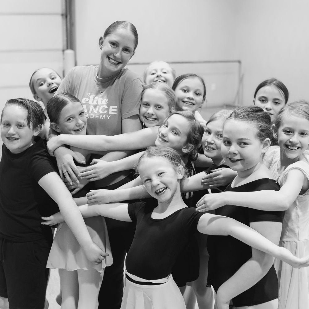 Smiling group of dance students hugging their dance teacher.