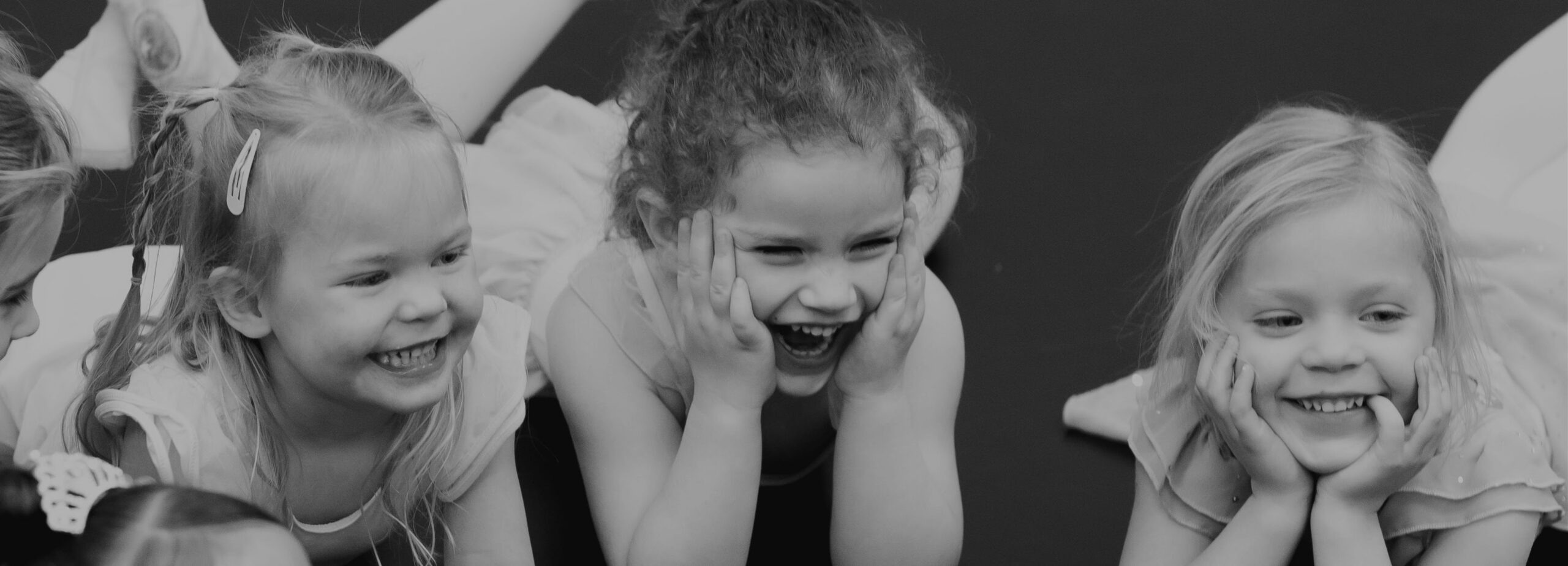 Three preschool dance students smiling while on the ground.